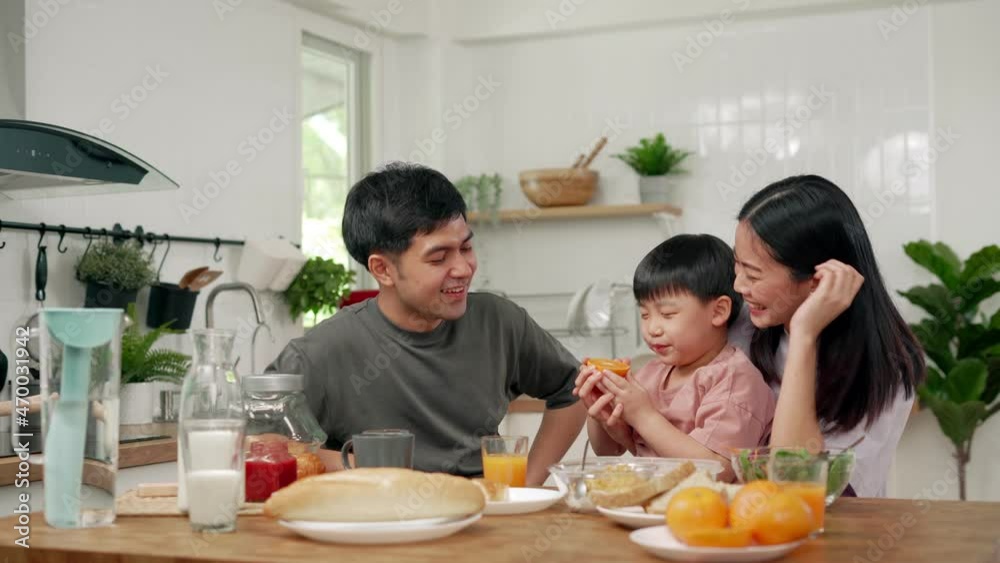 Asian family breakfast at home. Parents and children enjoy eating together, talking with laughter and good atmosphere. Father plays with son playfully at kitchen table. happy family day Asian family breakfast at home. Parents and children enjoy eating together, talking with laughter and good atmosphere. Father plays with son playfully at kitchen table. happy family day