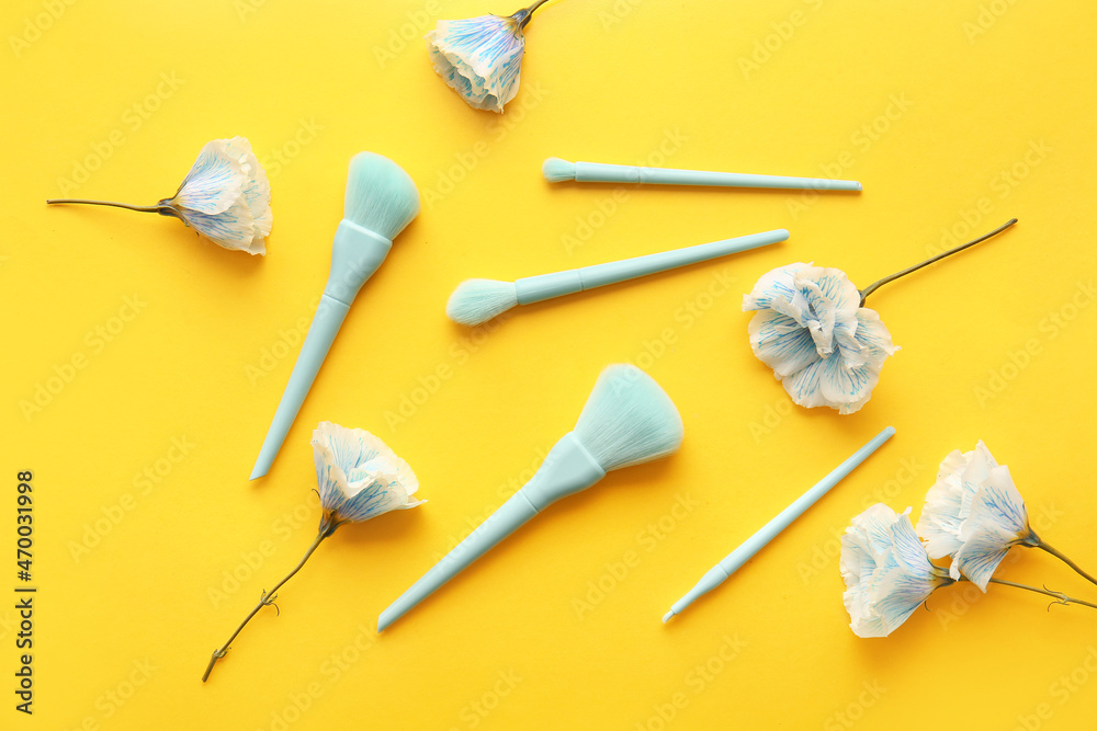 Set of stylish makeup brushes and flowers on yellow background Set of stylish makeup brushes and flowers on yellow background