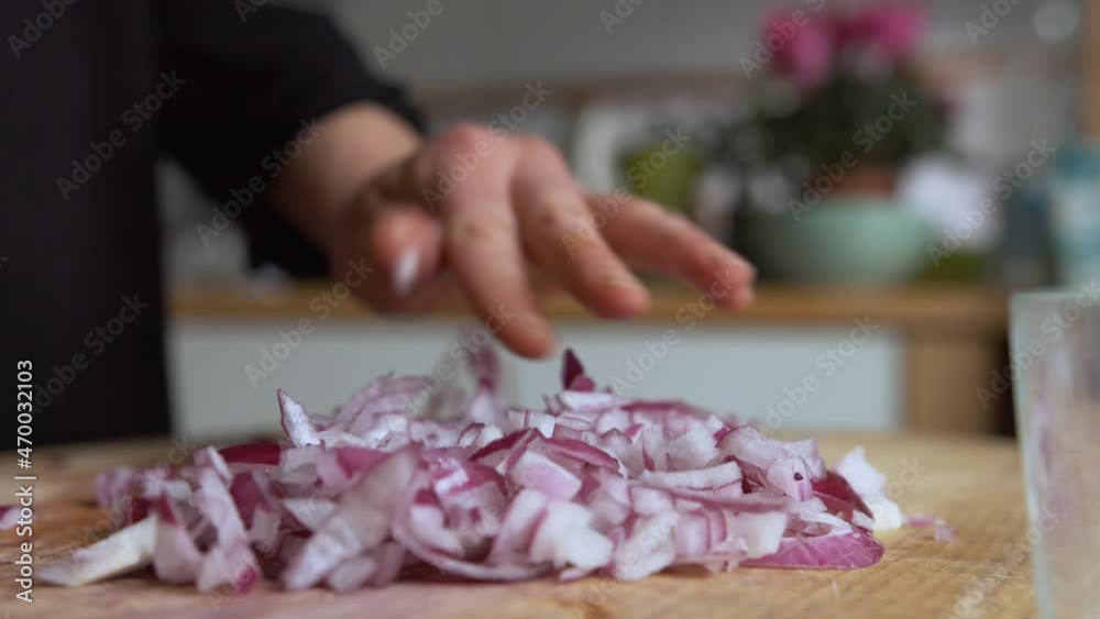 Close up pan woman's hand chopping Italian red onions with a rounded sharp knife on a wooden board in her kitchen, then slowly filling glass lunch box. Home cooking and healthy food concept Close up pan woman's hand chopping Italian red onions with a rounded sharp knife on a wooden board in her kitchen, then slowly filling glass lunch box. Home cooking and healthy food concept