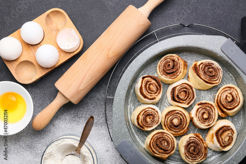 Baking dish of uncooked cinnamon rolls and ingredients on black and white background