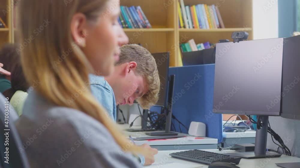Male university or college student working at computer in library being helped by tutor holding digital tablet - shot in slow motion Male university or college student working at computer in library being helped by tutor holding digital tablet - shot in slow motion