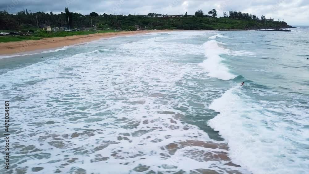 Aerial view of a surfer riding waves at a beach in cloudy Kauai, Hawaii - tracking, drone shot Aerial view of a surfer riding waves at a beach in cloudy Kauai, Hawaii - tracking, drone shot