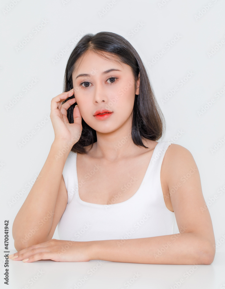 Portrait close up studio shot of millennial Asian short black hair model wearing makeup red lip in tank top undershirt sitting at table posing holding hand on cheek look at camera on white background Portrait close up studio shot of millennial Asian short black hair model wearing makeup red lip in tank top undershirt sitting at table posing holding hand on cheek look at camera on white background