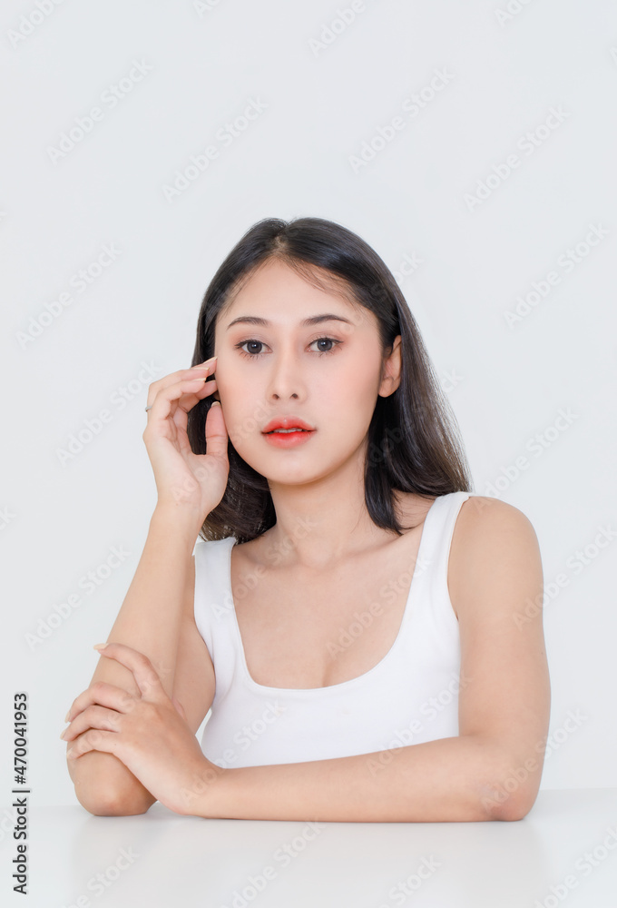 Facial beauty shot of Asian short black hair model with makeup red lipstick in tank top vest undershirt sitting at table posing crossed arm look at camera on white background Facial beauty shot of Asian short black hair model with makeup red lipstick in tank top vest undershirt sitting at table posing crossed arm look at camera on white background