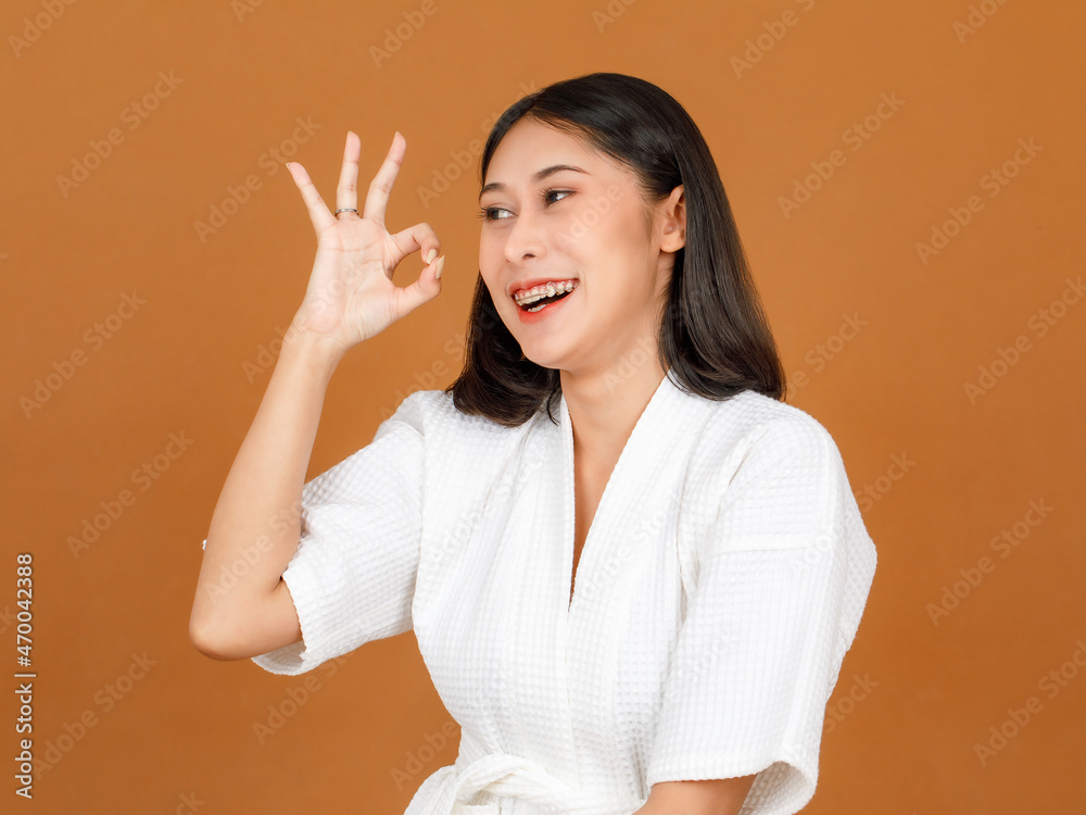 Portrait closeup studio shot of millennial Asian black short hair female model wearing makeup in white shower rope standing smiling look at camera posing holding ok hand sign up on brown background Portrait closeup studio shot of millennial Asian black short hair female model wearing makeup in white shower rope standing smiling look at camera posing holding ok hand sign up on brown background