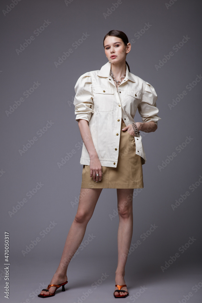 High fashion photo of a beautiful elegant young woman in a pretty white shirt, beige sand skirt, accessories posing on gray background. Studio Shot. Slim figure. High fashion photo of a beautiful elegant young woman in a pretty white shirt, beige sand skirt, accessories posing on gray background. Studio Shot. Slim figure.