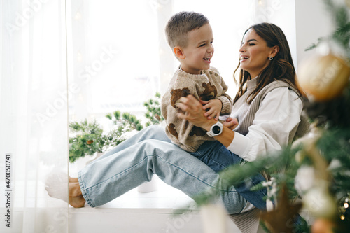 Happy mother with son sit on windowsill near Christmas tree photo