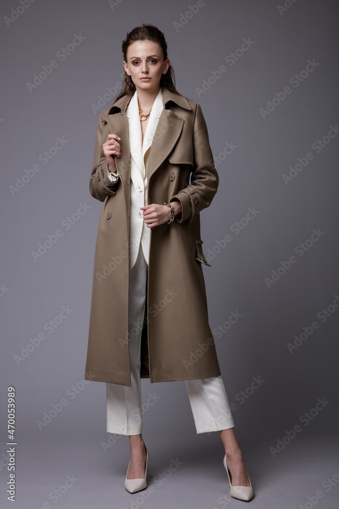 High fashion photo of a beautiful elegant young woman in a pretty dark beige, brown suit, accessories, white handbag posing on gray background. Studio Shot. Slim figure. High fashion photo of a beautiful elegant young woman in a pretty dark beige, brown suit, accessories, white handbag posing on gray background. Studio Shot. Slim figure.