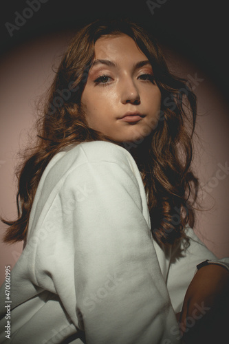 Young pretty woman in white sweater with curly hair opposite the lantern, on the pink background photo