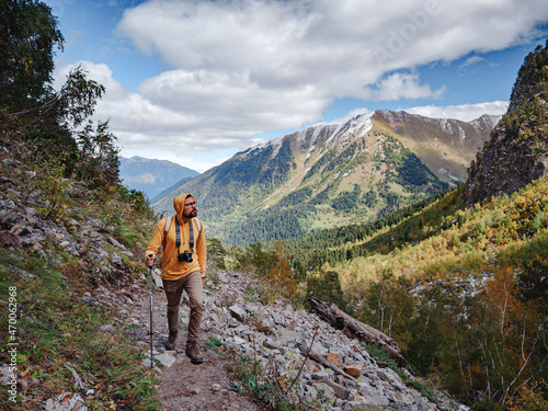 travel to Caucasus mountains in Karachay-Cherkessia, Arkhyz. Man in yellow hipster hoodie with photocamera hiking in mountains with travel backpack. Wandering lifestyle, adventure concept autumn