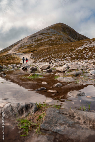 Couple of women walking on a path to the top of Croagh Patrick mountain. County Mayo, Ireland. Popular landmark for pilgrimage and hiking. Clean cloudy sky. Peak reflection in a puddle of water. photo