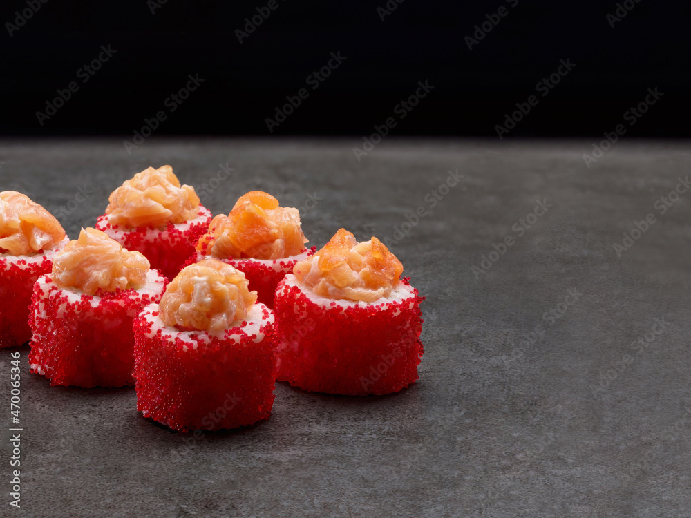 Japanese sushi roll with red flying fish roe. Asian dish pieces with salmon fillet pieces on top on dark concrete background. Copy space image. Single object. Inside out sushi
