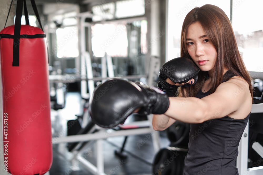 Portrait asia woman with black boxing gloves and red punching bag wearing sportswear in fitness or gym center, Strength sporty female and weight loss concept