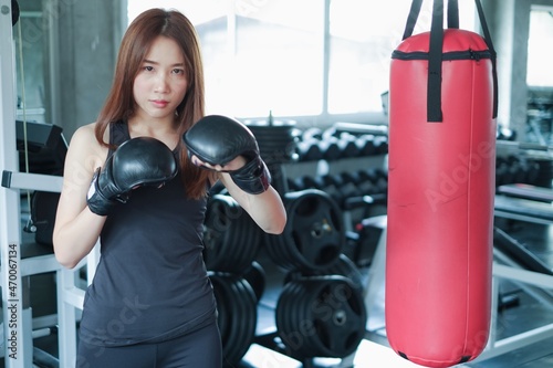 Portrait asia woman with black boxing gloves and red punching bag wearing sportswear in fitness or gym center, Strength sporty female and weight loss concept © u photostock