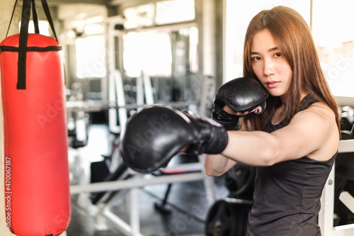 Portrait asia woman with black boxing gloves and red punching bag wearing sportswear in fitness or gym center, Strength sporty female and weight loss concept © u photostock