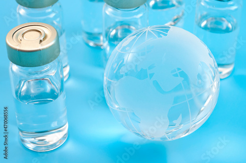 Global vaccines supply, international medical emergency and worldwide vaccination effort concept with glass globe and vaccine doses isolated on blue background