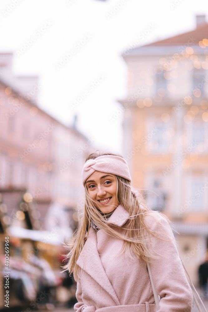 Blond hair girl enjoying the European Christmas market. Blurred lights on background