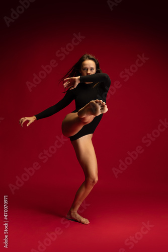 One emotional young flexible contemp dancer, ballerina jumping isolated on dark red background. Art, beauty, inspiration concept. © master1305