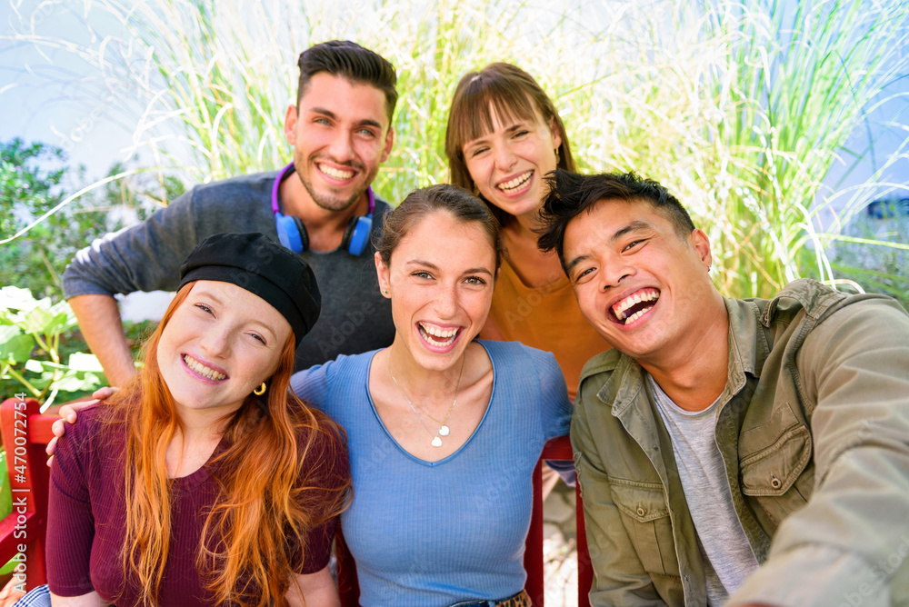 Obraz premium Positive young diverse friends smiling while taking selfie in garden