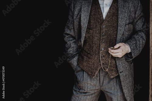 A man in a gray tweed suit and a brown vest holds a retro watch on a chain. Men's clothing banner with space for text for your ad
