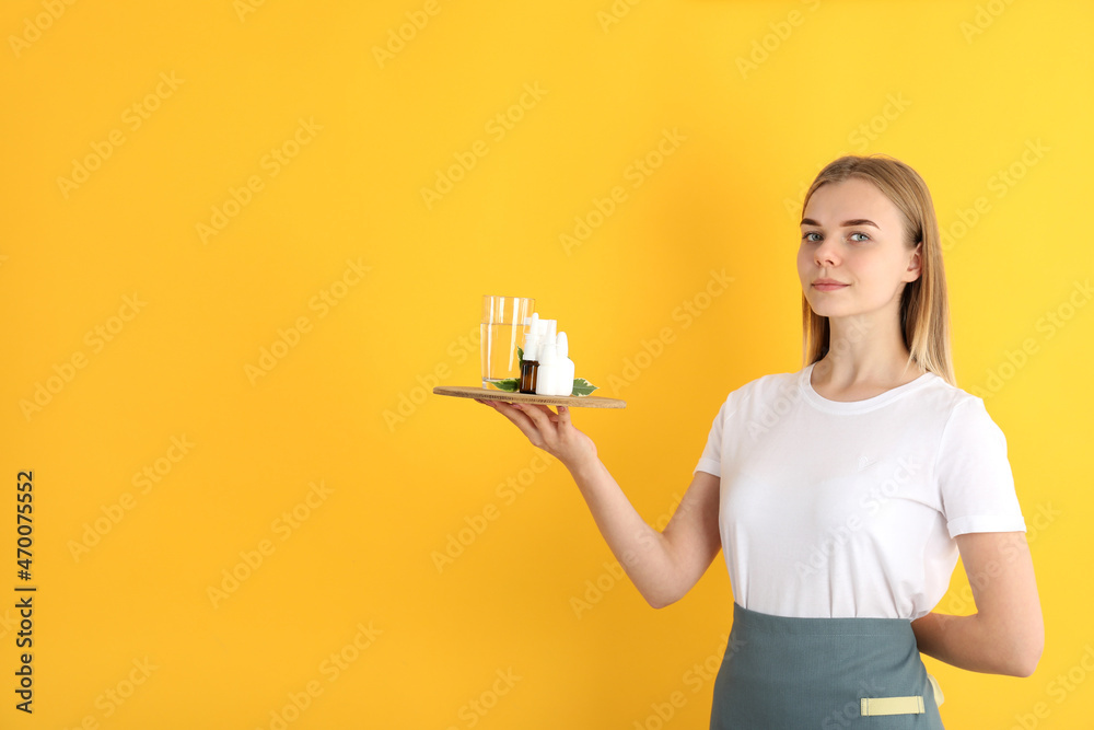 Young woman waiter holds tray with medicines on yellow background