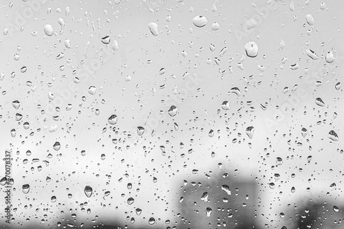 Rain drops on window glasses surface with gray sky and buildinhs background. The concept of bad rainy weather. photo