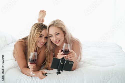 two sexy caucasian women holding selfie stick and a glass of wine