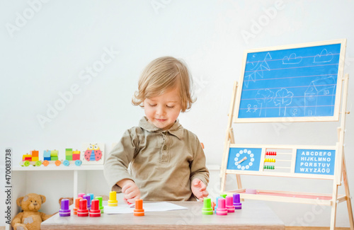 Cute little child having fun at home playing with colorful stamps on paper. Indoor activity for kids.