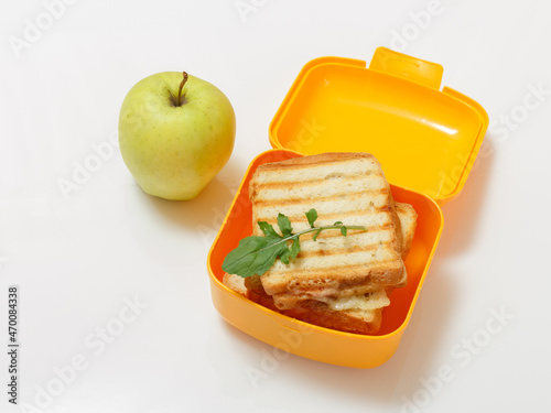 Yellow lunch box with toasted slices of bread, cheese and green parsley.