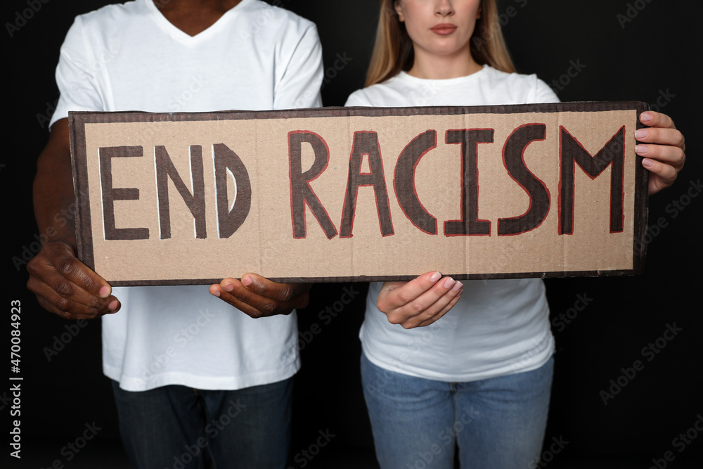 Young woman and African American man holding sign with phrase End Racism on black background, closeup Young woman and African American man holding sign with phrase End Racism on black background, closeup