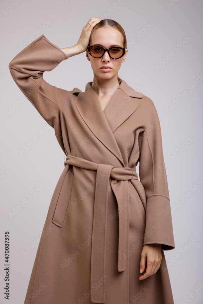 High fashion photo of a beautiful elegant young woman in a pretty beige brown autumn coat, stylish sunglasses posing on white background. Studio Shot. Slim figure. High fashion photo of a beautiful elegant young woman in a pretty beige brown autumn coat, stylish sunglasses posing on white background. Studio Shot. Slim figure.