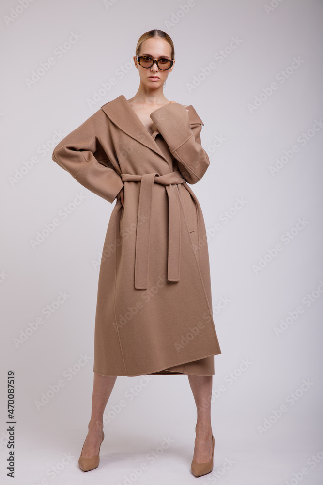 High fashion photo of a beautiful elegant young woman in a pretty beige brown autumn coat, stylish sunglasses posing on white background. Studio Shot. Slim figure. High fashion photo of a beautiful elegant young woman in a pretty beige brown autumn coat, stylish sunglasses posing on white background. Studio Shot. Slim figure.