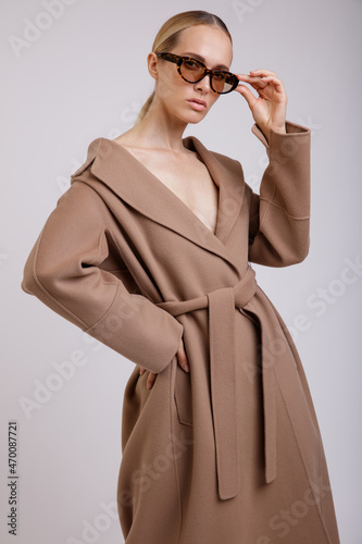 High fashion photo of a beautiful elegant young woman in a pretty beige brown autumn coat, stylish sunglasses posing on white background. Studio Shot. Slim figure.
