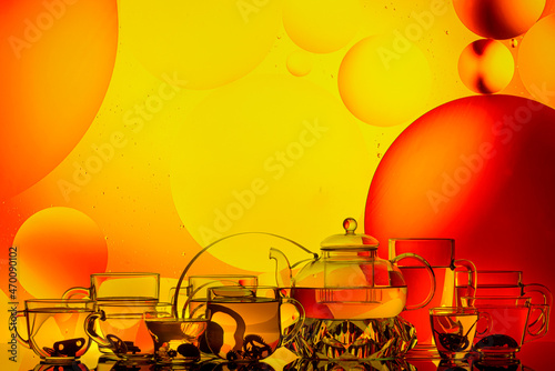 transparent glass teapot and cups with tea and drops on colorful background 