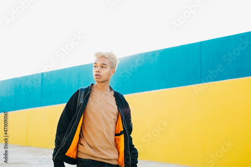 Young latin american  male walking on the street against a blue and yellow background