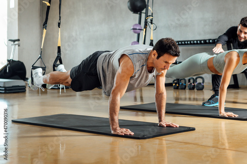 Strong man performing plank pose, suspensions training exercise at gym. photo