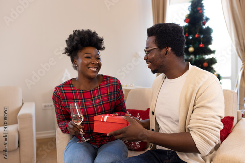 Man surprise woman for Chrismas. Cropped shot of a man surprising his girlfriend with a Christmas gift. Man giving a Christmas present to his girlfriend, Cheerful man and woman opens Christmas gift