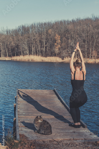 A woman with a cat doing yoga in nature by the river. The cat repeats yoga poses photo