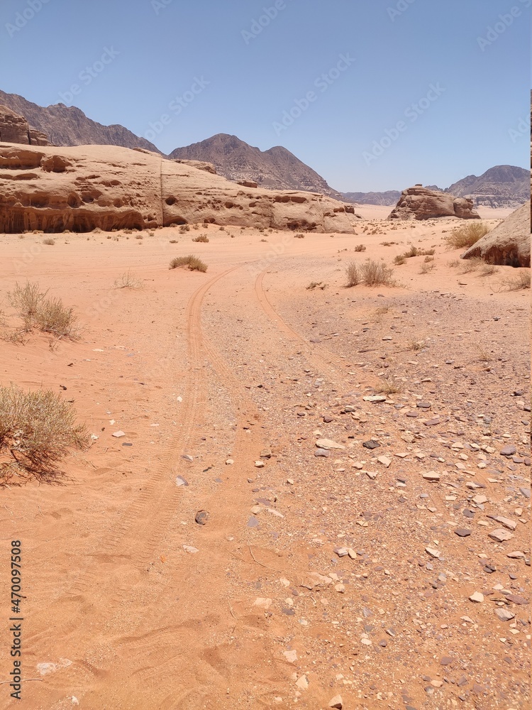 	 Dans la zone protégée du désert de Wadi Rum en Jordanie, avec de hautes montagnes rocheuses, exploration dans l'inconnu, sous un soleil et forte chaleur, tas de rochers, chemin avec trace de pneu