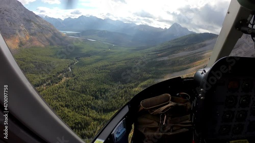 Inside of pilot flying a helicopter on autumn forest with turquoise lake in rocky mountains photo