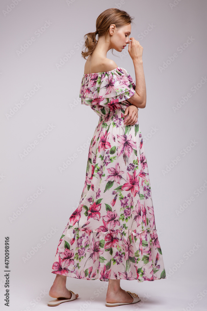 Fototapeta premium High fashion photo of a beautiful elegant young woman in pretty long dress with floral patterns in red color posing over white, soft gray background. Slim figure. Studio Shot. Femininity, tenderness
