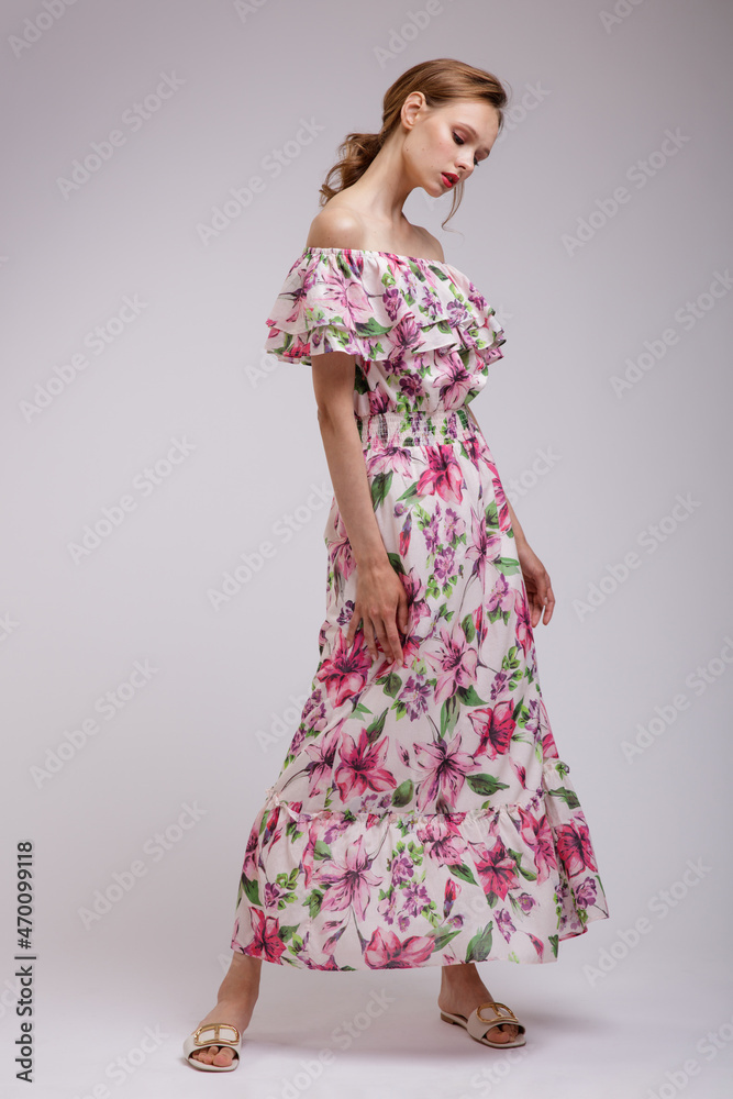 Naklejka premium High fashion photo of a beautiful elegant young woman in pretty long dress with floral patterns in red color posing over white, soft gray background. Slim figure. Studio Shot. Femininity, tenderness