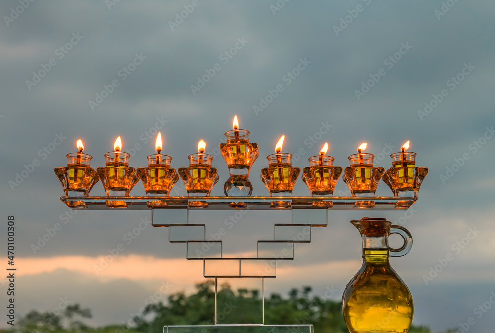 Obraz premium Crystal festive menorah and burning candles with olive oil as symbol of Hanukkah - Jewish Holiday of Miracle Light. Blurred background of evening overcast sky