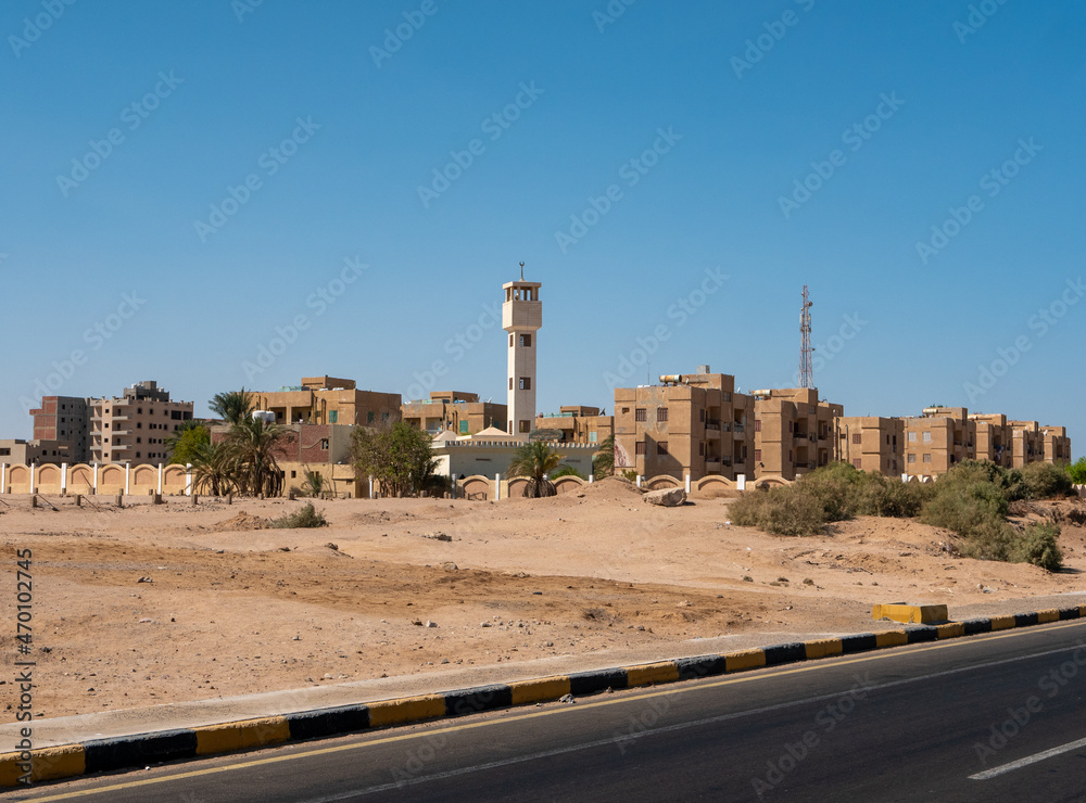 View from the road to the low houses of local residents surrounded by desert and palm trees against the background of a blue sky. Copy space. Safaga, Egypt.