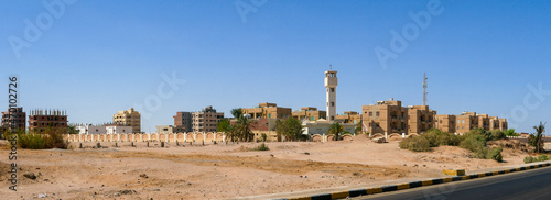 Panoramic view from the road to the low houses of local residents surrounded by desert and palm trees against the background of a blue sky. Copy space. Safaga, Egypt.