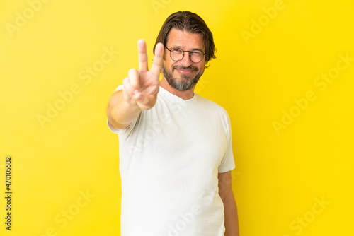 Senior dutch man isolated on yellow background smiling and showing victory sign