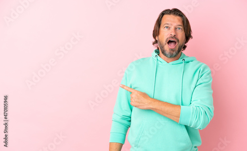 Senior dutch man isolated on pink background surprised and pointing side