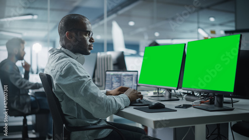 Multi-Ethnic Office: Black IT Programmer Working on Computer with Green Screen Chroma Key Display. Male Software Engineer Developing App, Program, Video Game. Terminal with Code Language.