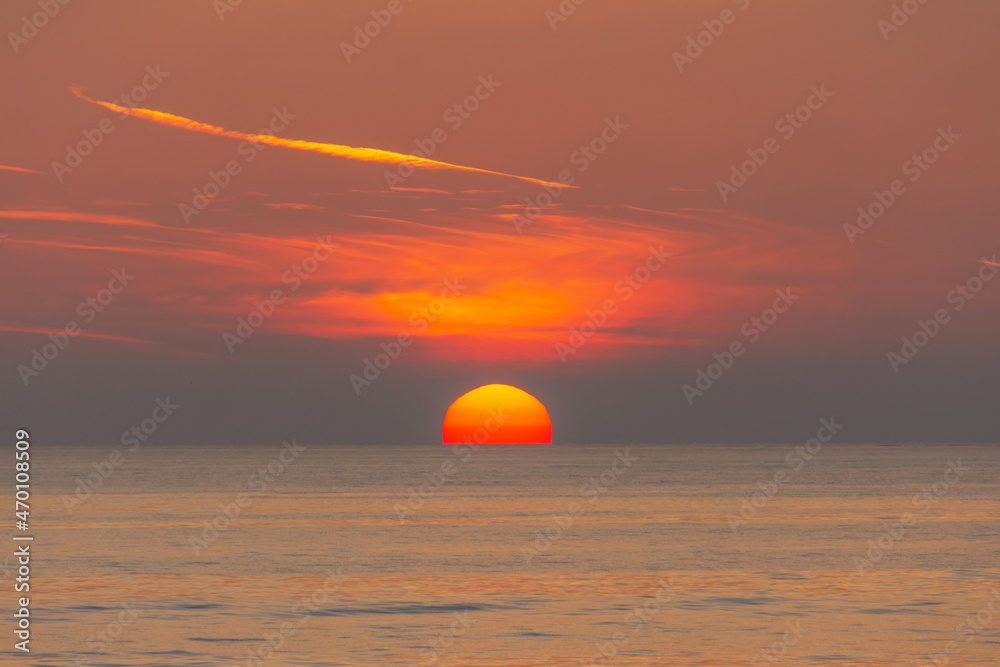 The sun's disk sets over the sea horizon.