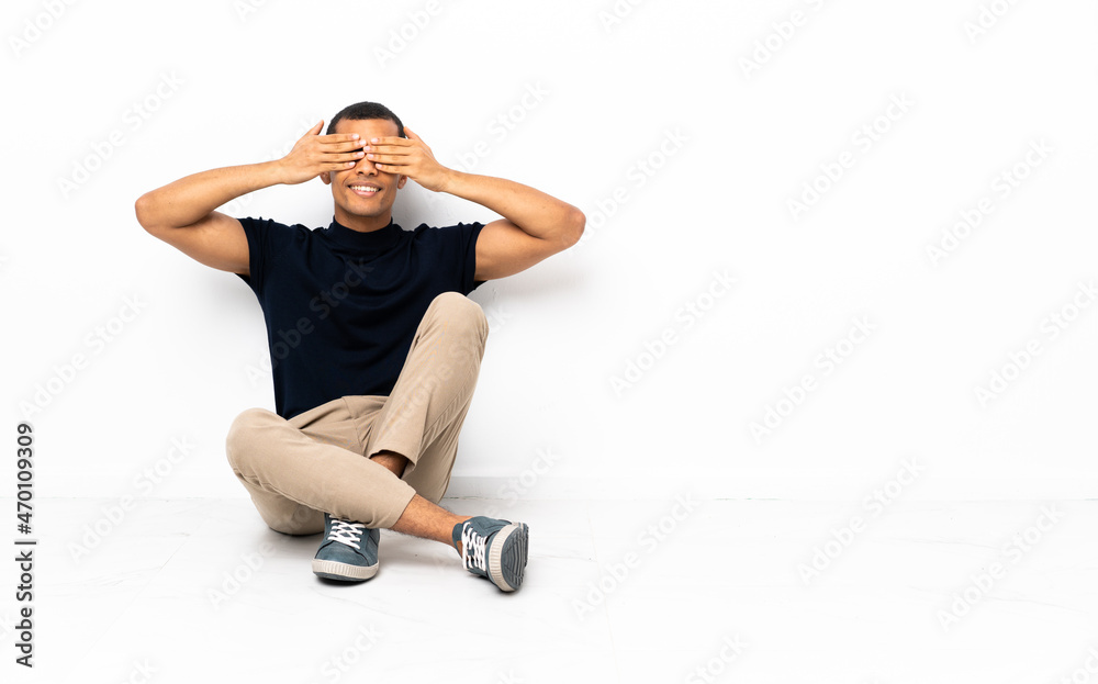 African American man sitting on the floor covering eyes by hands